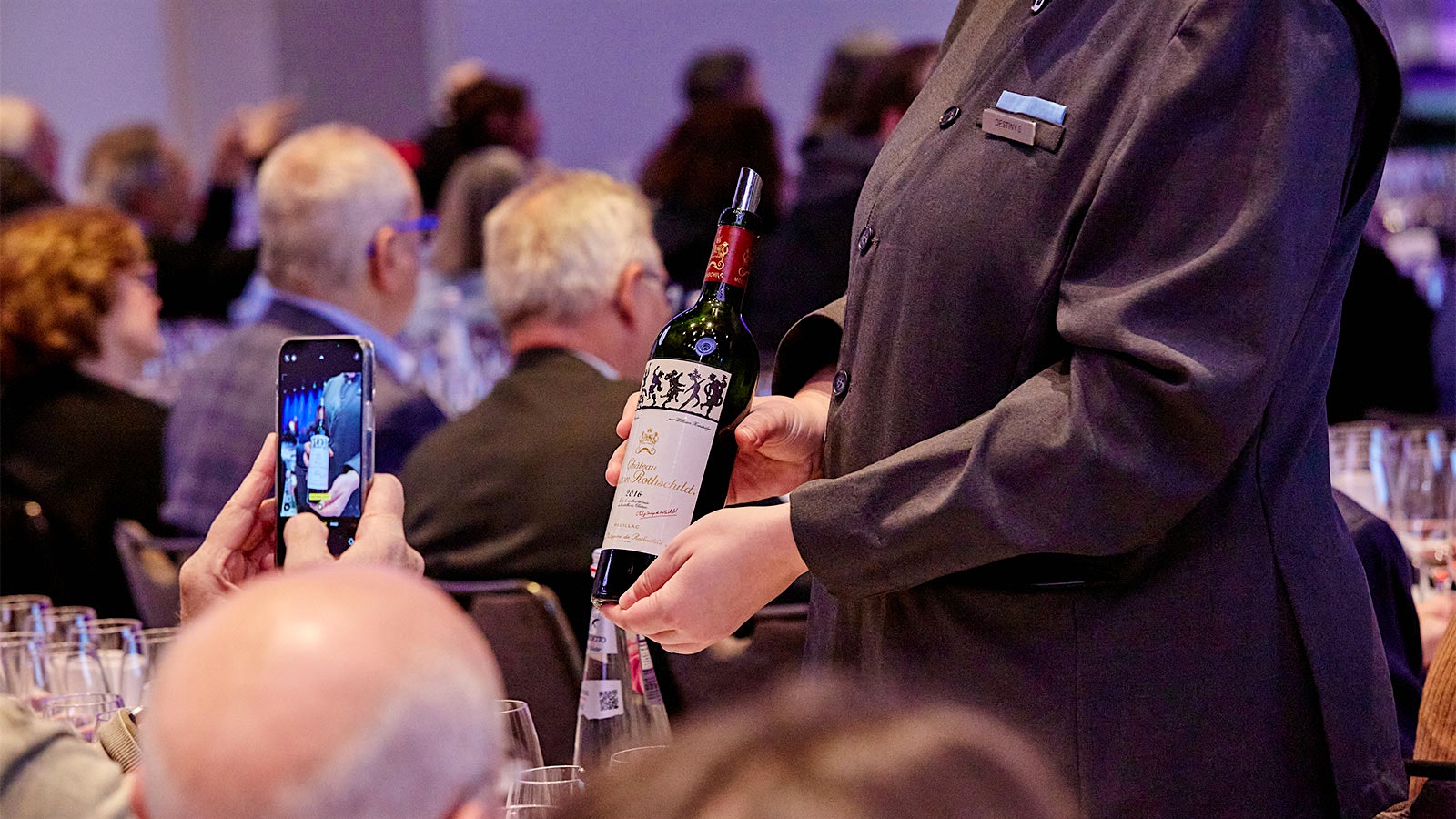 Guest taking a photo while a server pours a bottle of 2016 Château Mouton-Rothschild at the 2022 New York Wine Experience